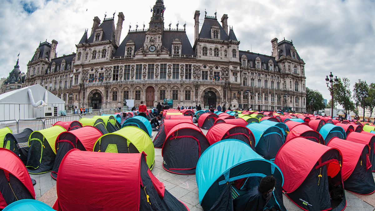 Homeless migrants sit in tents installed in front of the City Hall in Paris.