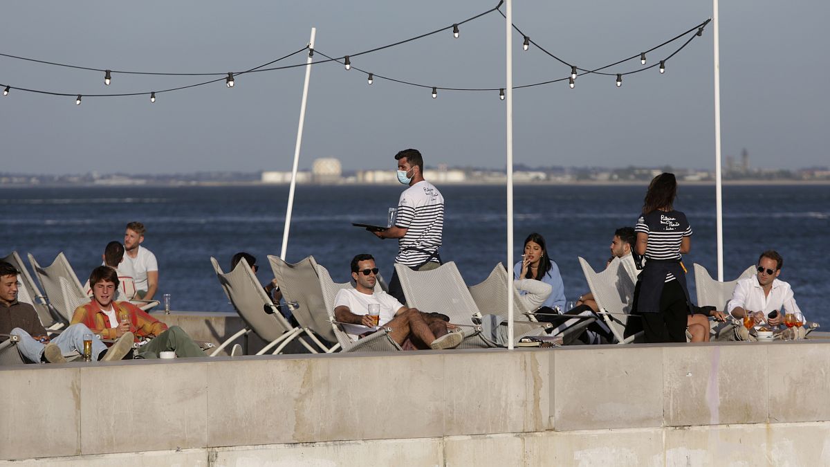 In this Friday, June 4, 2021 file photo, people have drinks by the Tagus river in Lisbon as the sun sets.
