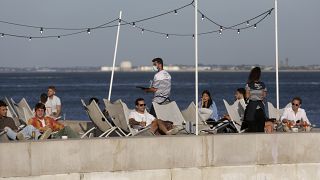 In this Friday, June 4, 2021 file photo, people have drinks by the Tagus river in Lisbon as the sun sets.