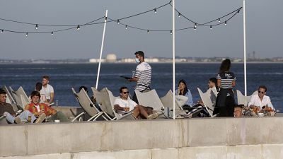 In this Friday, June 4, 2021 file photo, people have drinks by the Tagus river in Lisbon as the sun sets. In this Friday, June 4, 2021 file photo, people have drinks by the Tagus river in Lisbon as the sun sets.