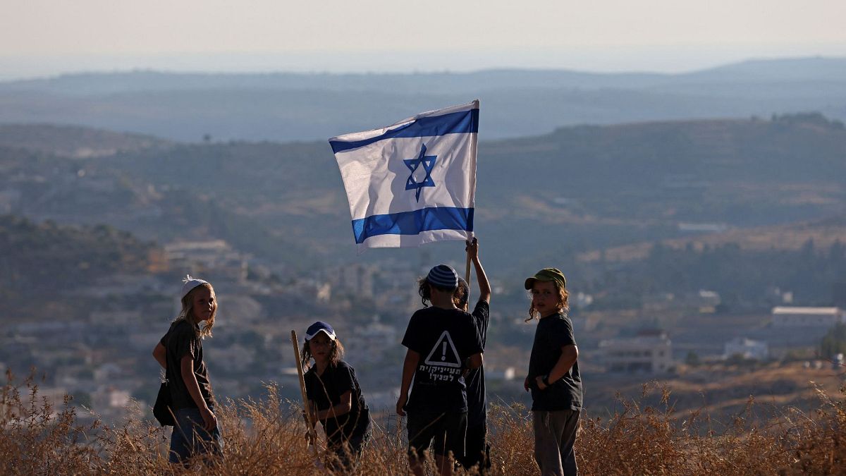 أطفال المستوطنين الإسرائيليين يلوحون بالعلم الوطني بالقرب من مستوطنة "بات عاين" في الضفة الغربية المحتلة، 21 يونيو 2021