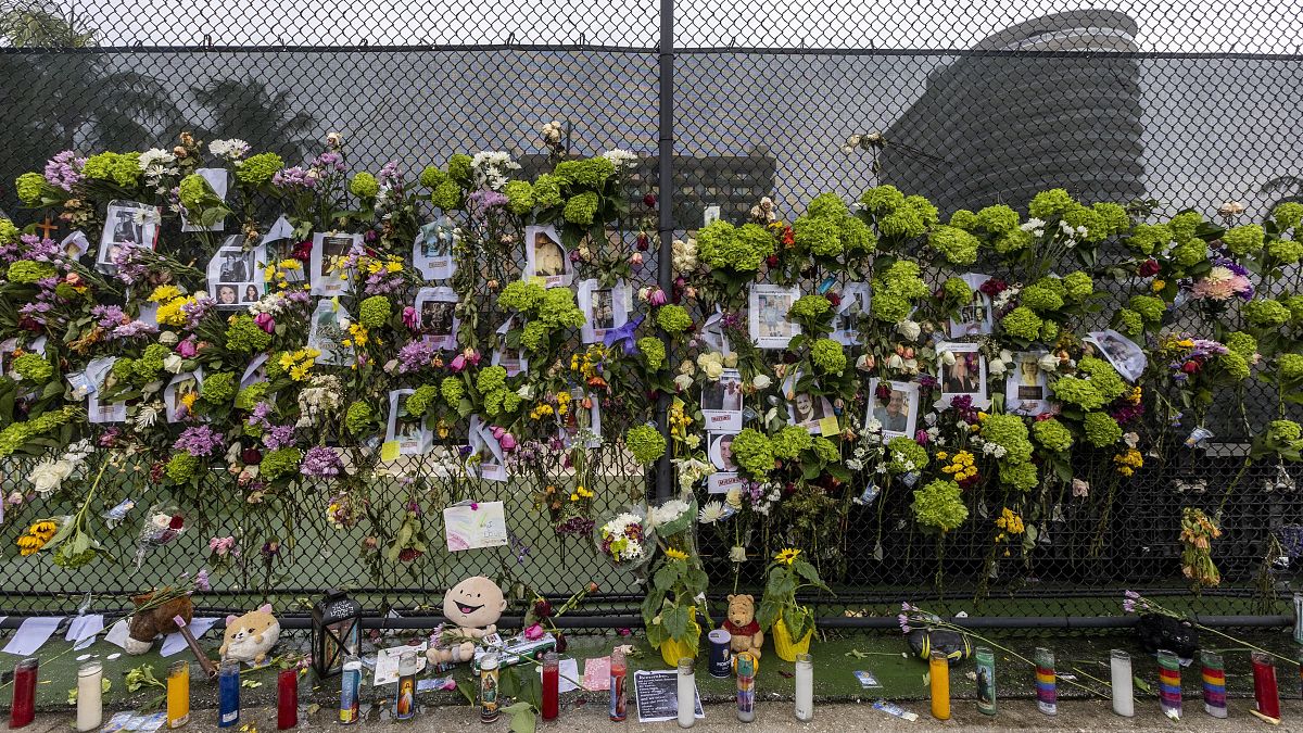 Flores y velas en honor de los desaparecidos junto a una valla cercana al edificio que se derrumbó parcialmente en Miami-Dade.