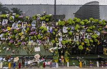 Flores y velas en honor de los desaparecidos junto a una valla cercana al edificio que se derrumbó parcialmente en Miami-Dade.