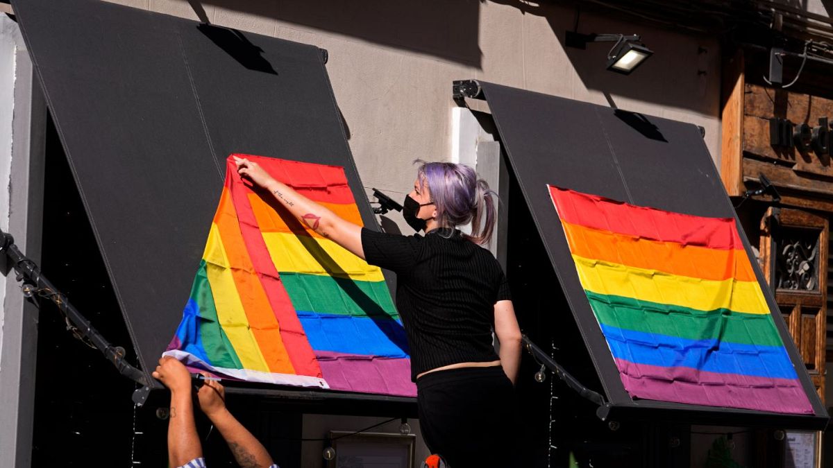 A woman hangs rainbow flags on the outside of a restaurant on the first day of the annual LGBT+ pride week in Madrid.