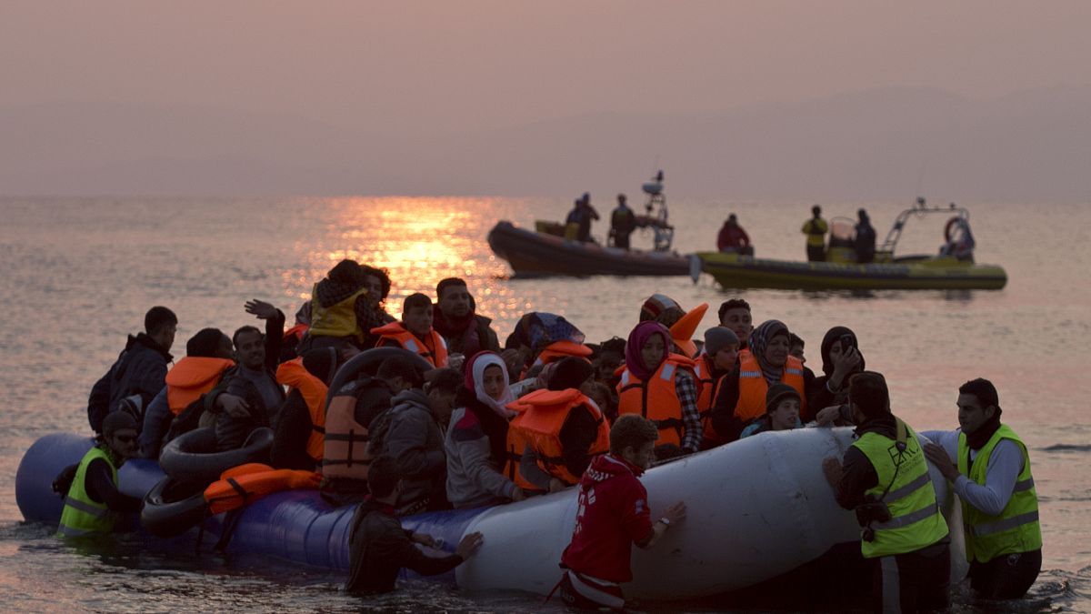 متطوعون يساعدون لاجئين ومهاجرين عند وصولهم إلى شاطئ جزيرة ليسبوس اليونانية بعد عبور بحر إيجه من تركيا، الأحد 20 مارس 2016