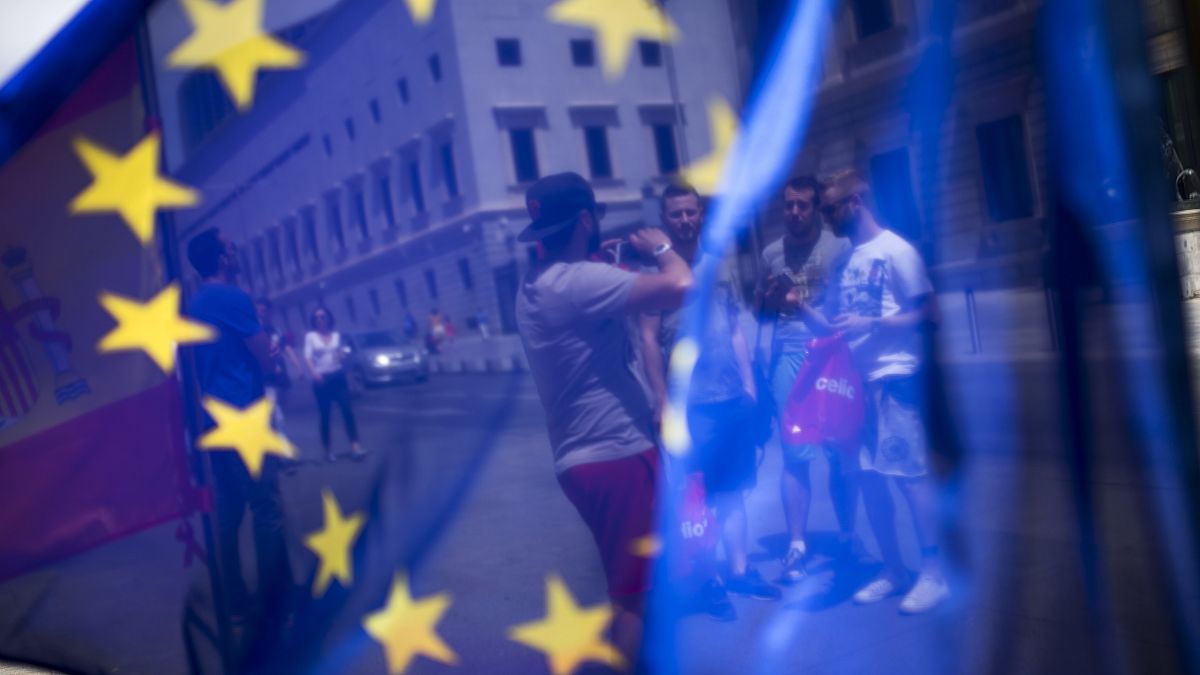 In this Friday, June 24, 2016 photo, a group of tourists posing for a photograph in front of the Spanish Parliament is seen through the EU flag in Madrid, Spain.