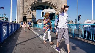 A woman shelters from the sun holding an umbrella, as she walks on Tower Bridge, in London.