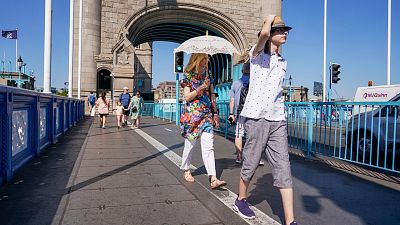A woman shelters from the sun holding an umbrella, as she walks on Tower Bridge, in London.
