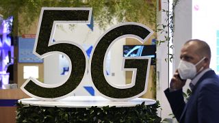 A man uses his phone next to a 5G logo at the Mobile World Congress (MWC) fair in Barcelon