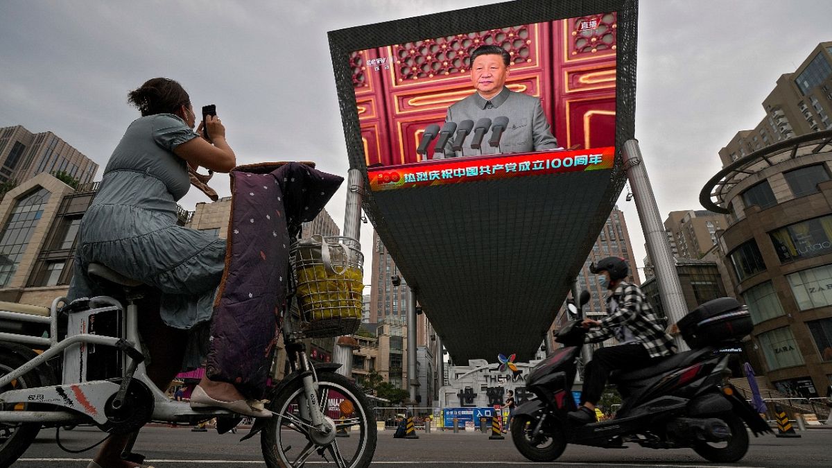 A woman films a large video screen showing Chinese President Xi Jinping's speech commemorating the 100th anniversary of China's Communist Party, Beijing, July 1, 2021.