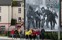 Tourists on a walking tour pass a mural depicting the 1972 Bloody Sunday killings, in the Bogside area of Derry, Northern Ireland, on March 13, 2019.