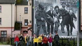 Tourists on a walking tour pass a mural depicting the 1972 Bloody Sunday killings, in the Bogside area of Derry, Northern Ireland, on March 13, 2019.