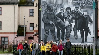 Tourists on a walking tour pass a mural depicting the 1972 Bloody Sunday killings, in the Bogside area of Derry, Northern Ireland, on March 13, 2019. Tourists on a walking tour pass a mural depicting the 1972 Bloody Sunday killings, in the Bogside area of Derry, Northern Ireland, on March 13, 2019.