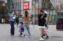 In this Monday, March 29, 2021 file photo, visitors to a shopping mall wearing masks stand before a Uniqlo store in Beijing.