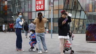 In this Monday, March 29, 2021 file photo, visitors to a shopping mall wearing masks stand before a Uniqlo store in Beijing.