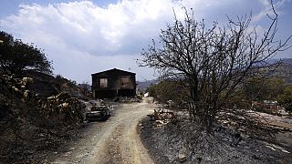 A burned car is seen outside a damaged house on Troodos mountain