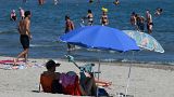 A man and a woman sit on the sand under a parasol on the beach in Palavas-les-Flots, southern France