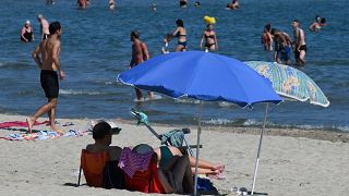 A man and a woman sit on the sand under a parasol on the beach in Palavas-les-Flots, southern France