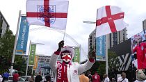 An England fan waves flags outside Wembley Stadium in London, Wednesday, July 7, 2021, ahead of the Euro 2020 soccer championship semifinal match between England and Denmark.