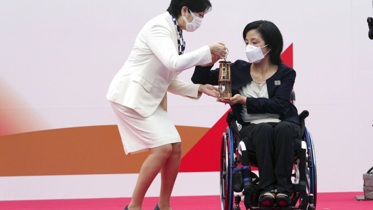 Tokyo Gov. Yuriko Koike, left, receives a lantern containing the Olympic Flame from Aki Taguchi