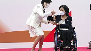 Tokyo Gov. Yuriko Koike, left, receives a lantern containing the Olympic Flame from Aki Taguchi