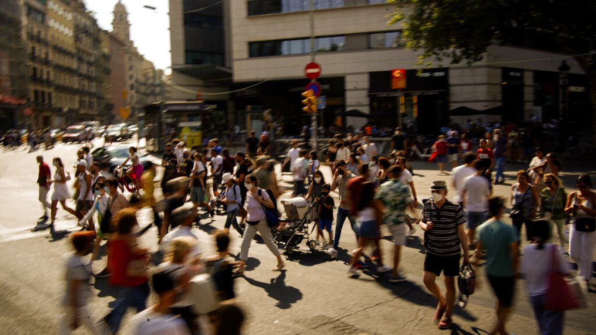 People wearing a face mask to protect against the spread of coronavirus walk along a street in downtown Barcelona, Spain, Saturday, July 3, 2021. 