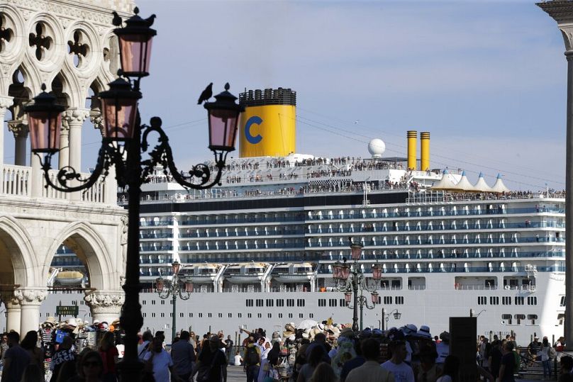 A cruise ship passes by St. Mark's Square filled with tourists.