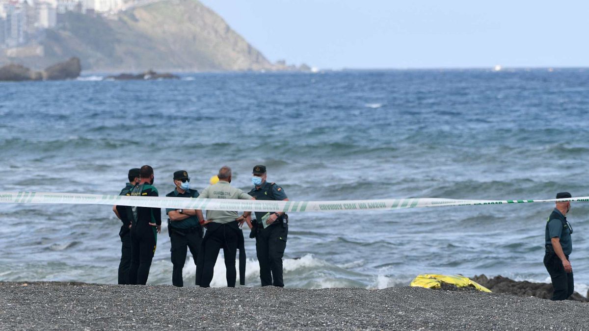 أعضاء الحرس المدني الإسباني يقفون بجوار جثة مهاجر على شاطئ جيب سبتة الإسبانية في 20 مايو 2021