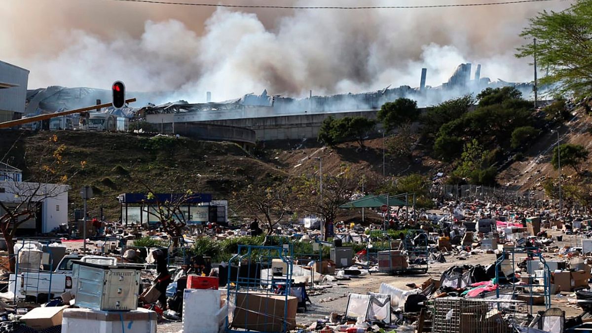 A factory burns in the background while empty boxes litter the foreground from looted goods being removed, on the outskirts of Durban, South Africa, Wednesday, July 14, 2021.