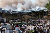 A factory burns in the background while empty boxes litter the foreground from looted goods being removed, on the outskirts of Durban, South Africa, Wednesday, July 14, 2021.