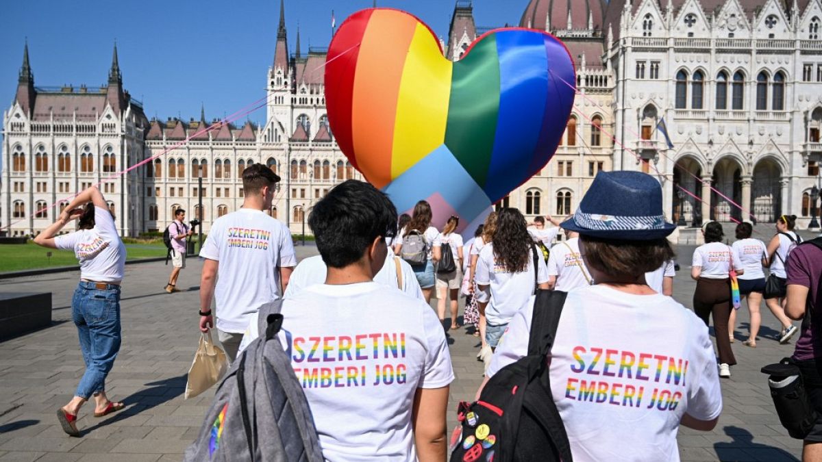 Activists wear shirts reading "Love is a human right" as they fly a giant heart balloon in rainbow colors in front of the parliament in Budapest