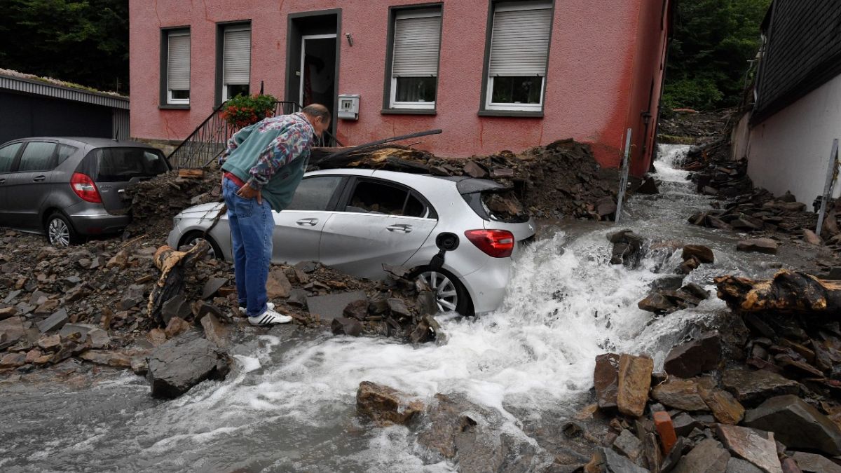 رجل ينظر إلى سيارة مغطاة بحطام ناجم عن الفيضانات، هاغن، ألمانيا، 15 يوليو 2021 