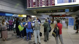 Passengers queue at the counter of Groundforce, a ground handling company at Lisbon airport, beneath a screen showing departing flights Saturday, July 17, 2021. 