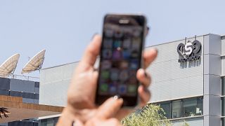أحدهم يستخدم هاتف "أيفون" ويظهر الخلفية المبنى الرئيسي لمجموعة "إن إس أو" الإسرائيلية المطورة لبرنامج التجسس "بيغاسوس"، مدينة هرتسيليا