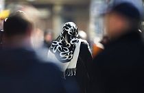 a woman with a headscarf, a traditional dress for Islamic women, walks between other people on a street at the district Neukoelln in Berlin.