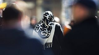 a woman with a headscarf, a traditional dress for Islamic women, walks between other people on a street at the district Neukoelln in Berlin.