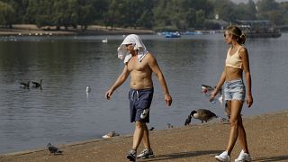 A man keeps cool with a shirt over his head as he walks alongside The Serpentine in Hyde Park in London, Aug. 12, 2020.