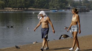 A man keeps cool with a shirt over his head as he walks alongside The Serpentine in Hyde Park in London, Aug. 12, 2020. 