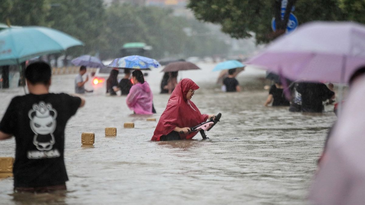 Des personnes pataugeant dans les eaux de crue le long d'une rue suite à de fortes pluies à Zhengzhou le 20 juillet 2021