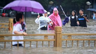 People walk through floodwaters along a street in Zhengzhou in central China's Henan Province, Tuesday, July 20, 2021. 