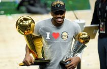 Giannis Antetokounmpo smiles while holding the NBA Championship trophy and Most Valuable Player trophy.