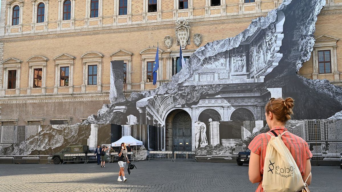 Des passants regardent l'oeuvre de JR sur la façade du palais Farnese à Rome