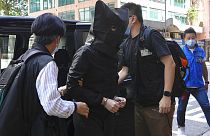 A hooded suspect is accompanied by police officers to search evidence at an office in Hong Kong, Thursday, July 22, 2021