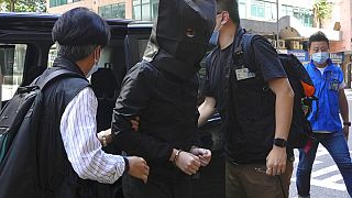A hooded suspect is accompanied by police officers to search evidence at an office in Hong Kong, Thursday, July 22, 2021