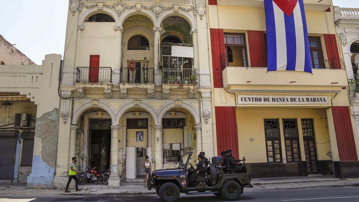 دورية للشرطة الكوبية أمام علم كوبي كبير يتدلى من واجهة مبنى في هافانا، كوبا.