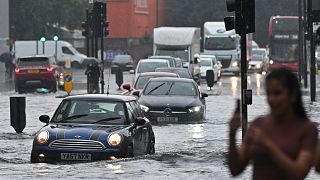 Cars are driven through deep water on a flooded road in The Nine Elms district of London on July 25, 2021 during heavy rain.