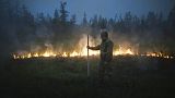 A member of volunteers crew walks past a burning grass near the edge of the fire at Gorny Ulus area west of Yakutsk, Russia, Thursday, July 22, 2021.