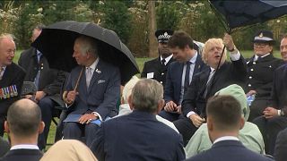  UK Prime Minister Boris Johnson struggles with umbrella as he sits with Prince Charles at a dedication ceremony for a police memorial.