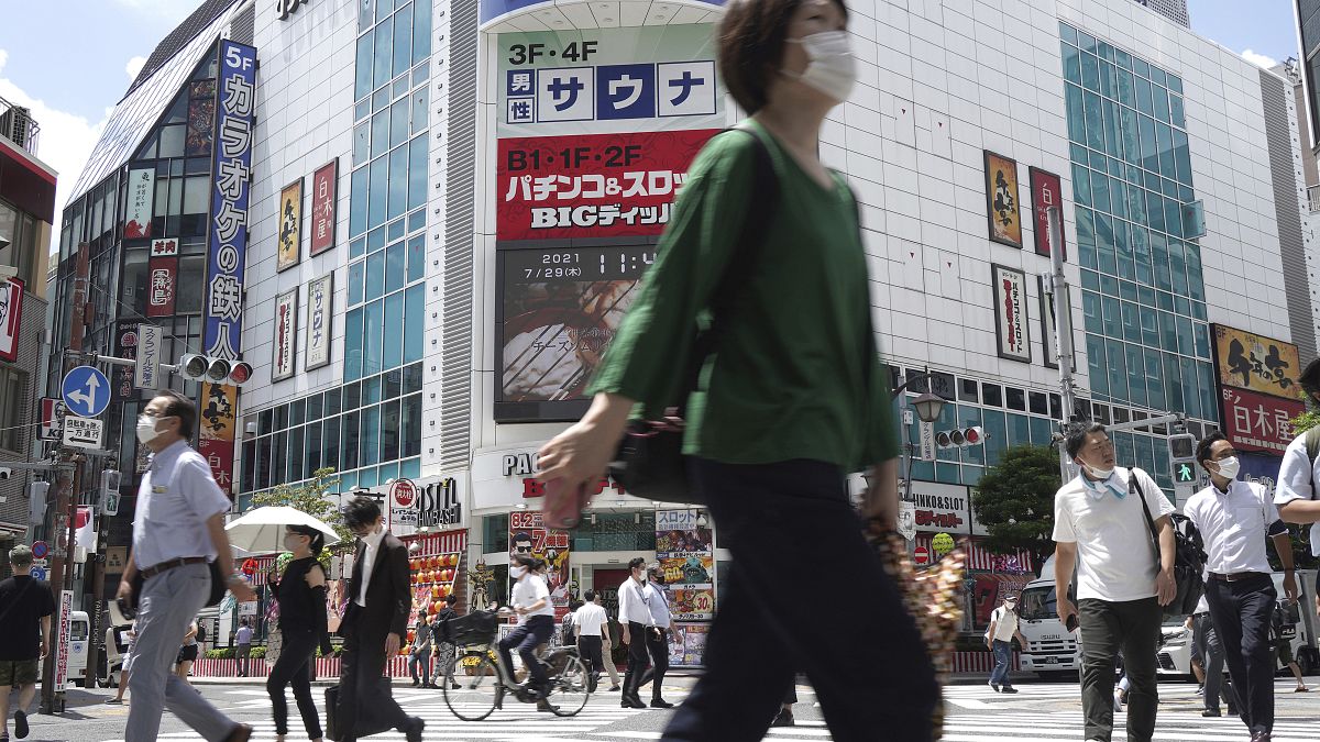 People walk across a crossing near Shimbashi Station in Tokyo Thursday, July 29, 2021, a day after the record-high coronavirus cases were found in the Olympics host city.