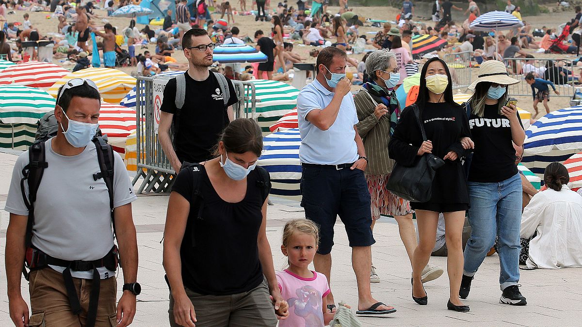 Persone che indossano maschere per proteggersi dal coronavirus camminano sulla passeggiata pedonale lungo la spiaggia di Biarritz, nel sud-ovest della Francia, 28 luglio 2021